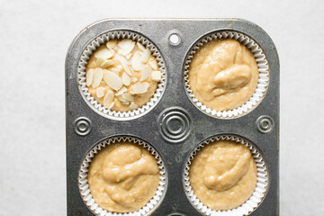 vanilla almond muffins batter in a cupcake pan, almond muffins topped with sliced almonds, process of making almond muffins