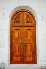 Old rustic castle door with round arch made of red-brown wood. Entrance area.
