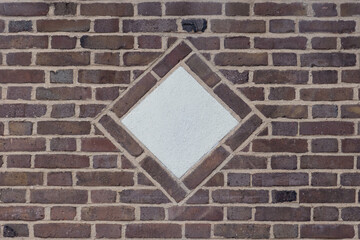 a decorative concrete diamond shaped medallion in the center of a rustic brown brick wall in flemish bond bricklay pattern, copy space