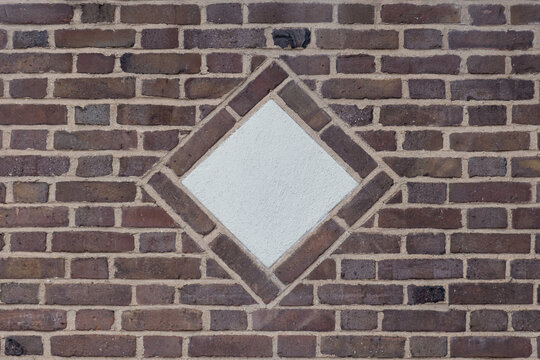 a decorative concrete diamond shaped medallion in the center of a rustic brown brick wall in flemish bond bricklay pattern, copy space