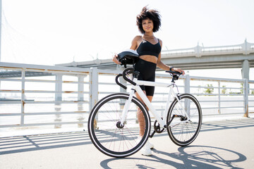 Sporty  woman with a stylish bike on a sunny bridge, ready for an urban cycling adventure.