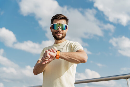 Athletic man in casual wear checking smartwatch outdoors, tech-savvy.