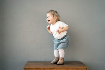 Joyful toddler dancing on a wooden bench in a playful pose, carefree.