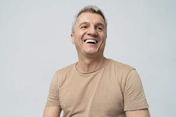 Cheerful mature man laughing heartily against a light background. - obrazy, fototapety, plakaty