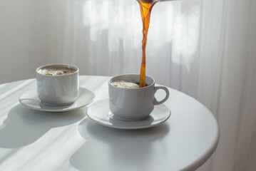 two white cups with coffee on white table