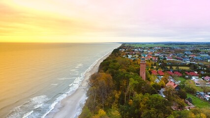 Captured by drone on a cloudy November day, the Gąski lighthouse stands against the somber sky. The tranquil sea with gentle waves laps an empty beach. © Grzegorz