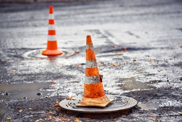 Foto auf Alu-Dibond Orange traffic cone stands on manhole. Road repair works, asphalt laying, pylon to mark an obstacle or hole on road. Traffic cone stands on hatch, asphalt paving works © Tricky Shark