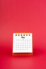 May 2024 white mini desk calendar on red background.