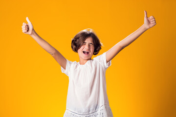 Smiling kid girl showing thumbs up gesture over yellow background. Success concept