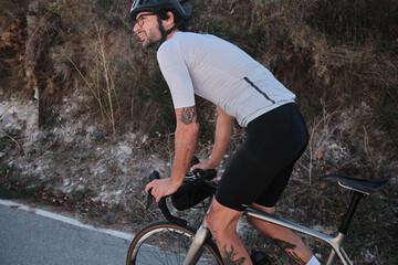 A man is riding a gravel bicycle on the road in the hills with a mountain view. Athlete wearing...