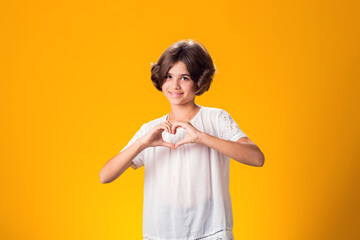 Smiling kid girl showing heart gesture over yellow background. Love concept