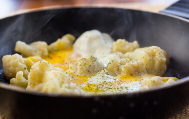 Cooked cauliflower, fried with eggs, in a frying pan with spices.