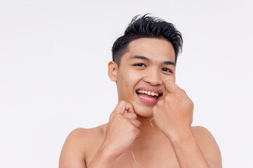 A young topless asian man flossing his teeth. Tooth care and grooming. Studio shot isolated on a white backdrop.