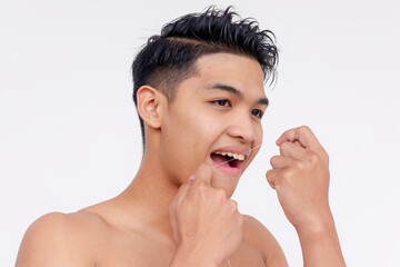 A young topless asian man flossing his teeth. Tooth care and grooming. Studio shot isolated on a white backdrop.