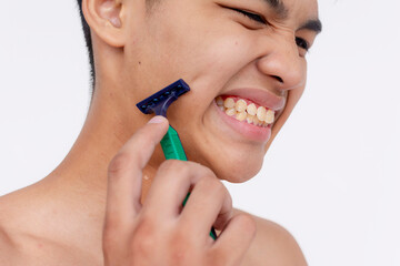 A young asian man feels irritated while using a disposable razor to cleanly shave the sideburns. Possible cut on the face. Closeup tight shot isolated on a white backdrop.