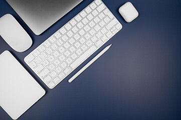 Top view of laptop computer, white keyboard, touchpad, mouse, earphones case and pen on dark blue background. Modern office flat lay, copy space. 