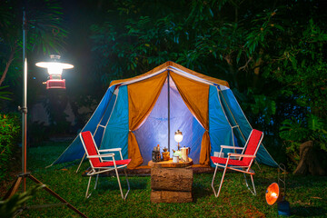 vintage cabin tent,  Antique oil lamp, retro chairs, Group of camping tents with outdoor coffee-making facilities on wooden tables in a forest camping area at night in the  forest - obrazy, fototapety, plakaty