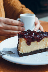 vertical image, slice of cheesecake with female hands holding cup of coffee blurred in background