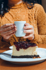 vertical image, slice of cheesecake with female hands holding cup of coffee blurred in background