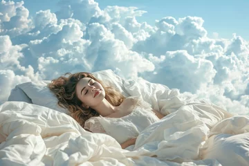 Deurstickers A young woman sleeps on a bed as soft as clouds in an airy and fluffy blanket. The girl smiles blissfully, experiencing the peace and pleasure of rest. © photolas
