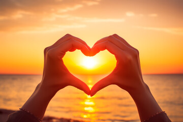 Closeup of the hands of a woman forming a heart during sunset in the beach. Love emotion.