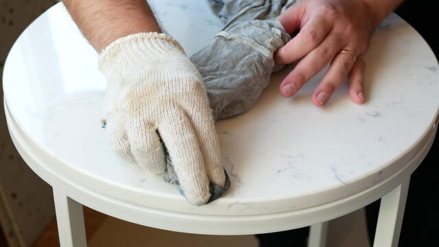 Person is wiping a surface of marbled round coffee table, selective focus. Process of making a handmade piece of furniture