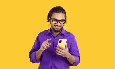 Young cheerful Indian man carefree uses phone playing games and reading entertainment content in...