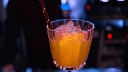Barman pouring orange red alcohol cocktail with ice on a bar with neon lights at night