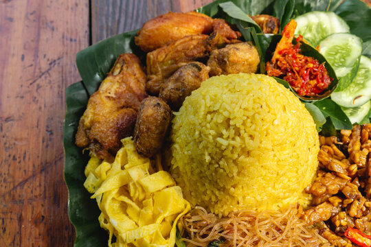 nasi kuning or nasi tumpeng, steam rice with turmeric, fried chicken, tempeh, sambal and fresh vegetables on top of banana leaves