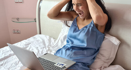 Screaming woman in bed in front of laptop monitor with bank card