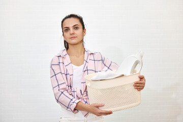 Woman is holding basket with laundry and detergent bottle, copy space