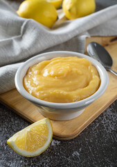 Homemade lemon curd or cream in bowl, with fresh lemons on a gray background.