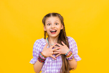 The child put on a lot of bracelets made of beads and beads. A happy little girl is enjoying a beaded ornament. Beading for children. Isolated yellow background.