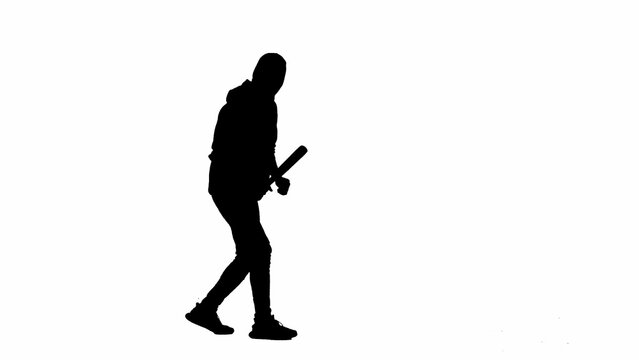 Black silhouette of thief on isolated white background. A male robber in hoodie and balaclava walks with a wooden club in his hands, preparing to commit a crime. Half-turn.