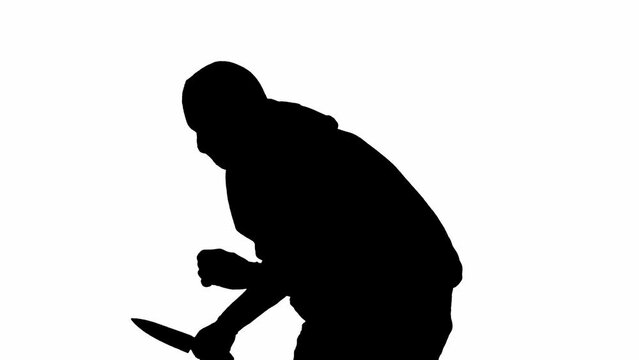Black silhouette of thief on isolated white background. A male robber in a hoodie and balaclava walks with a knife in his hands, preparing to commit a crime. Half-turn.