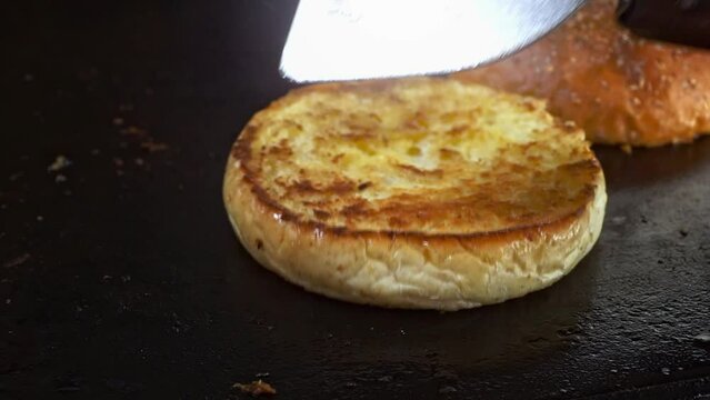 Toasting hamburger bun on a flat griddle, flipping golden crispy crust bun