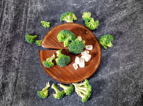 Inflorescences of green broccoli and garlic still life image. Wooden natural round stand. Top view.