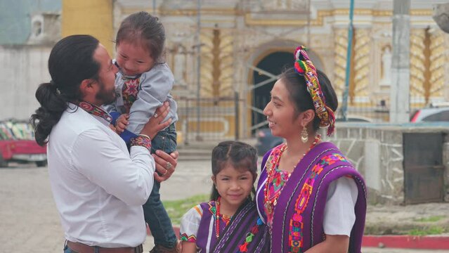 The family in front of the church enjoys a day of celebration. The father carries his son and plays with him, the mother and daughter look at the camera smiling.The family in front of the church enjoy