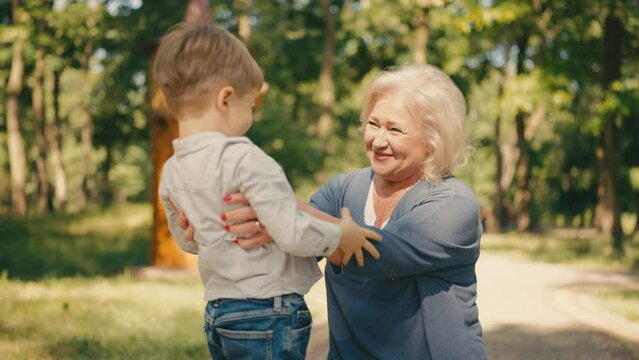 Loving grandma hugging little boy, having fun with grandson in summer park