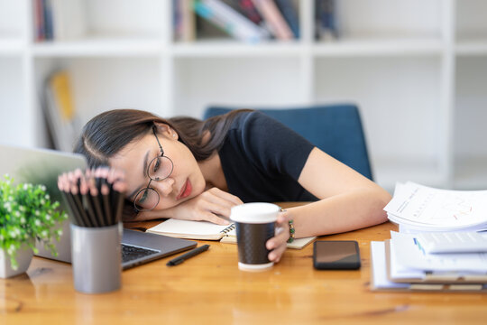 Freelance Asian businessperson, A businesswoman sits slumped on arm at her desk in a bored mood. Distracted while taking a break from  busy schedule.