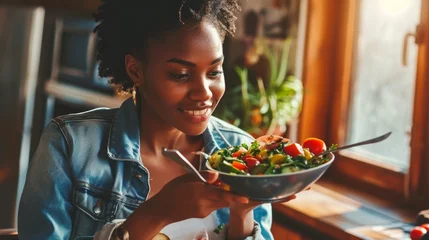 Poster Beautiful afro american woman eating vegetable salad at home. © Emil