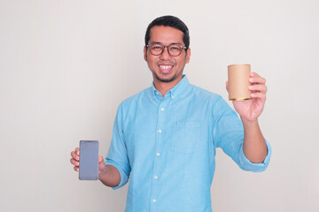 Adult Asian man smiling while showing a canned product and holding blank mobile phone screen