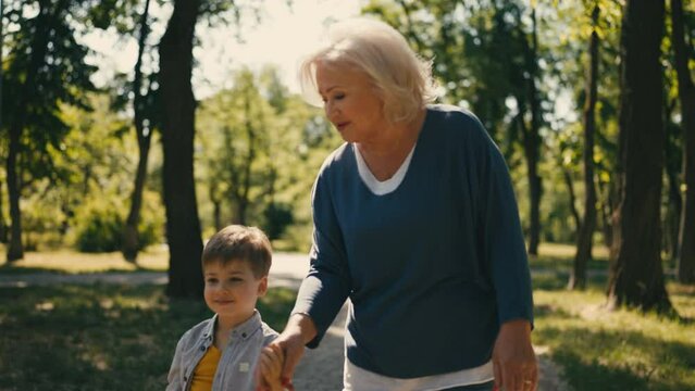 Happy senior woman walking in park with little grandson, leisure together