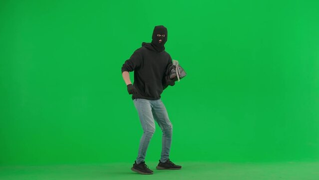 Portrait of thief on chroma key green screen background. Man robber with stolen bag walks, got caught up, standing on knees holding hands up.