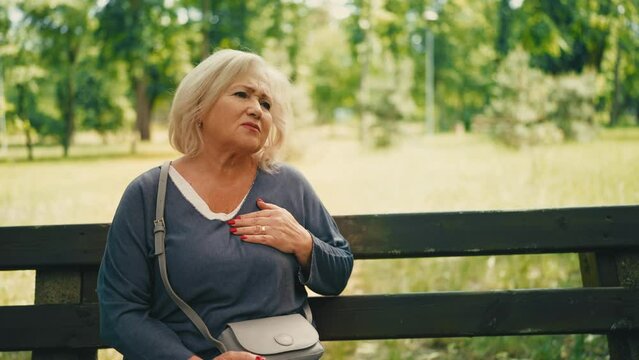 Distressed senior woman suffering chest pain, having panic attack in park