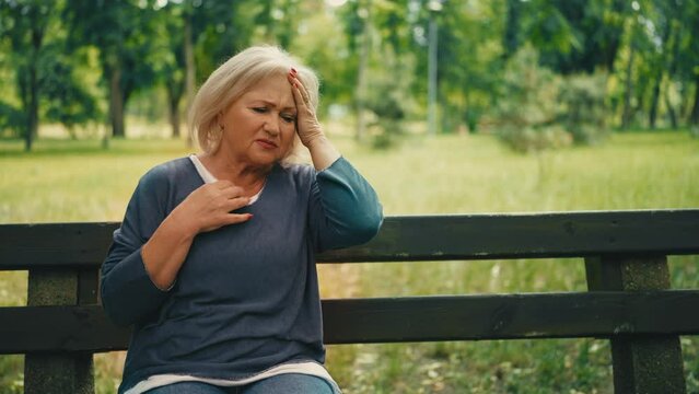 Adult woman suffering hot flush, sitting on bench in park, menopause symptom