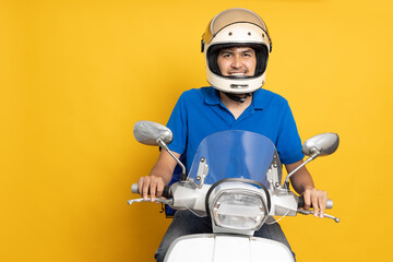 Delivery man wearing blue uniform riding motorcycle and delivery box isolated on yellow background....