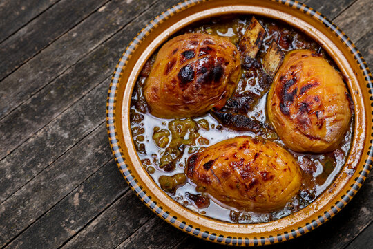 Moroccan lamb with quice tagine dish in open traditional tagine pot on rustic wooden table.