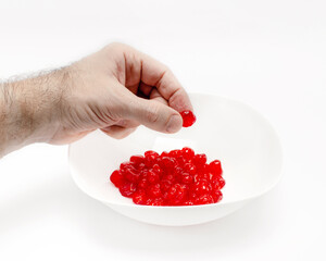 Man's hand holds a cherry over a white bowl with delicious red dried cherries. White background.