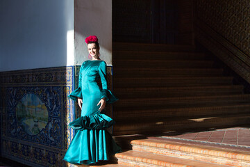 Young and beautiful woman with green frilly dress and dancing flamenco is on the stairs of plaza de espana in seville, andalusia. The woman has art and is typical of spain.